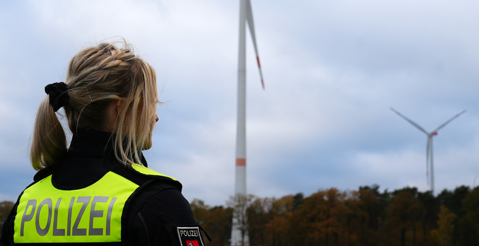 Polizistin steht vor Windkraftanlage